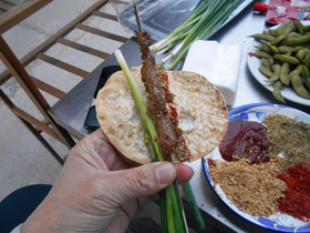 たれと香辛料を付けた煎饼（ジィェンビン）に焼いた食材とねぎを挟んで包み、串を引き抜く。